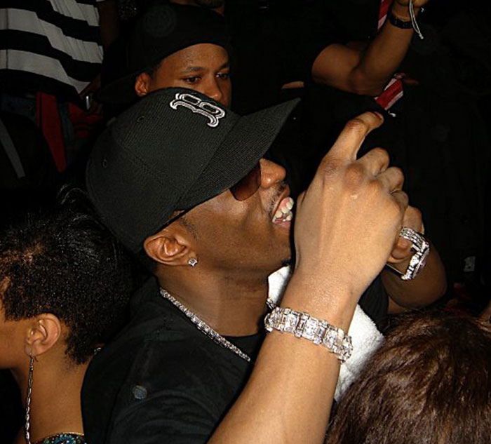 Man in a black cap and sunglasses at a lively event, possibly linked to celebrity secrets and scandals.