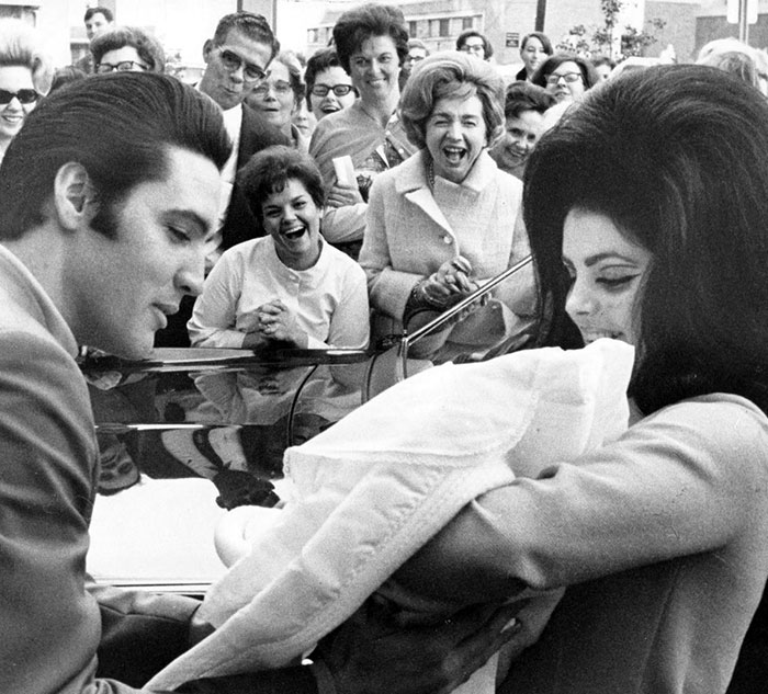 Black and white photo showing a man and woman with a baby in a crowd, reflecting celebrity secrets and scandals theme.