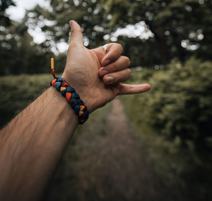 Man on a forest path wearing a colorful braided bracelet, gesturing with a thumbs-up, illustrating common scams awareness.