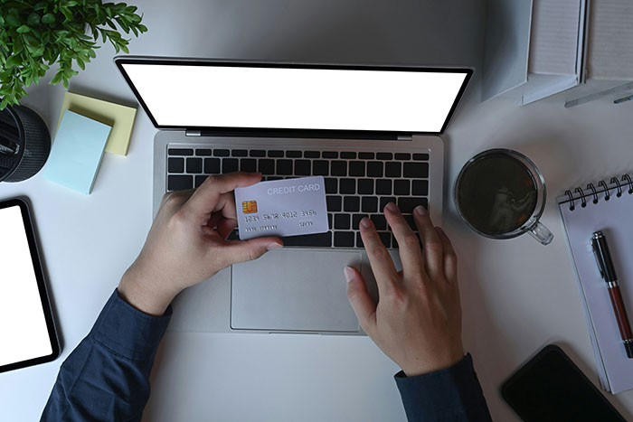 Person holding a credit card in front of a laptop, highlighting common scams in America.