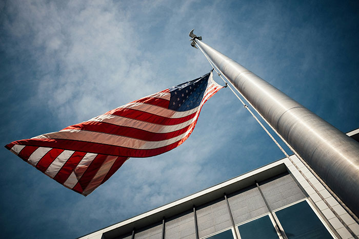 American flag waving on a tall flagpole against a clear blue sky, symbolizing common scams in America.