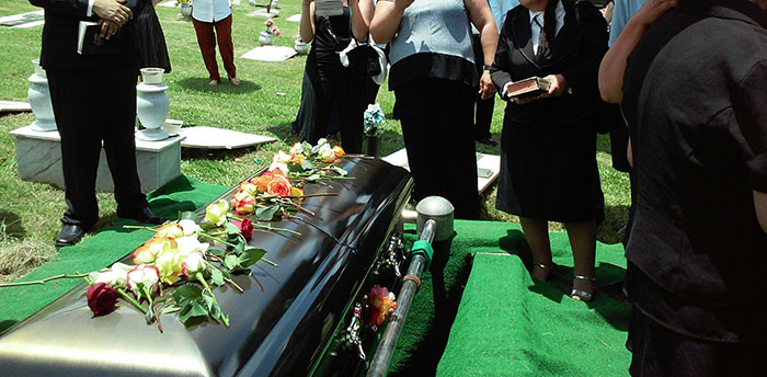 A funeral scene with a casket and flowers, surrounded by people in formal attire, symbolizing scams in America.