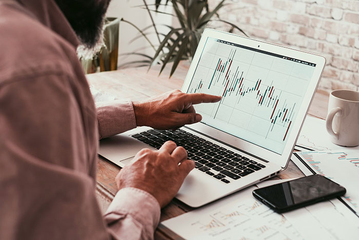 Man analyzing graphs on a laptop screen, pointing at data related to common scams in America.