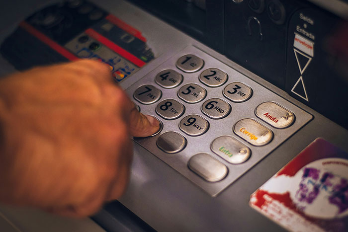 Hand pressing ATM keypad, illustrating common scams in America.