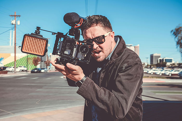 Person holding a professional camera on an urban street, capturing footage.