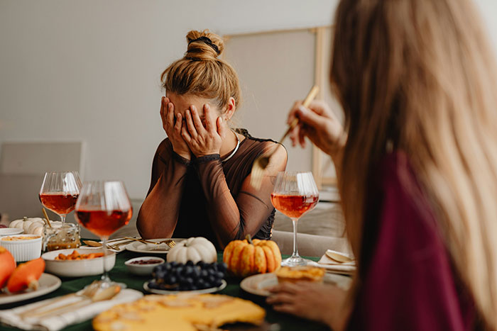 People at a dinner table with food and drinks, one person covering their face.