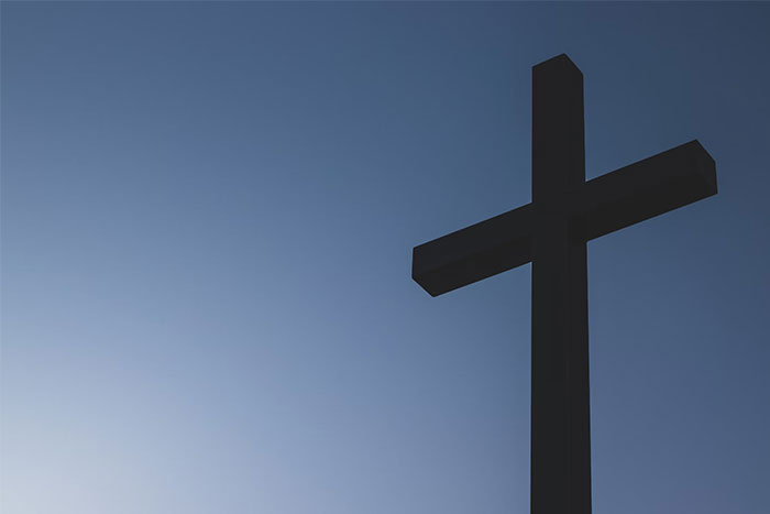 Silhouette of a large cross against a clear blue sky, symbolizing collective effort.