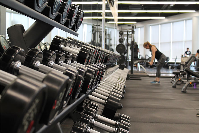 Gym with rows of dumbbells and a person exercising, reflecting wasted money on unused fitness equipment.