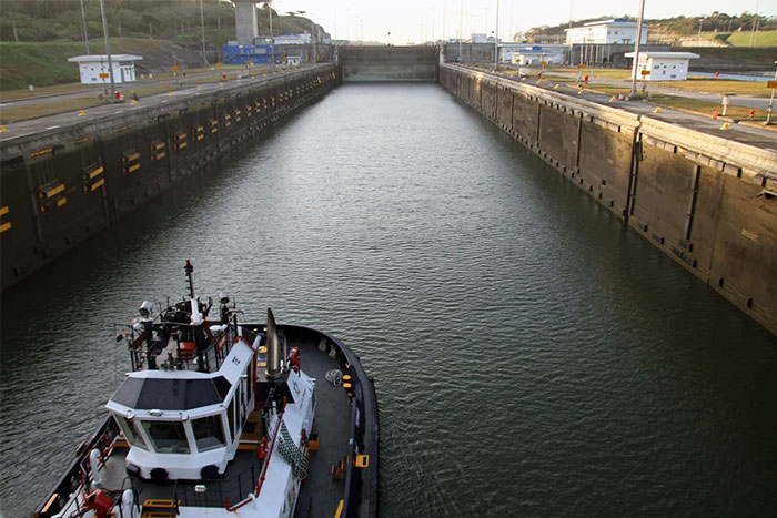 A tugboat navigates through large canal locks, illustrating extensive money waste on infrastructure projects.