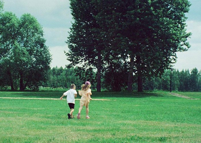 Children playing in a grassy field under large trees, possibly depicting unsolved mysteries.