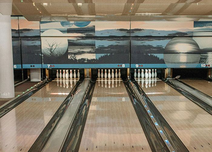 Bowling alley lanes with pins set up, featuring mysterious landscape mural in the background.