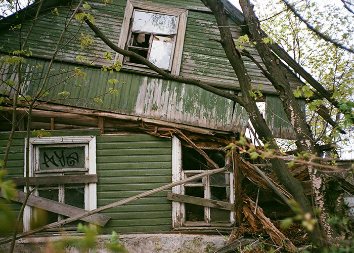 Dilapidated green house with broken windows and graffiti, surrounded by trees, illustrating unsolved mysteries.