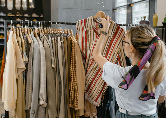 Woman browsing clothes on a rack in a store, looking at a striped shirt.