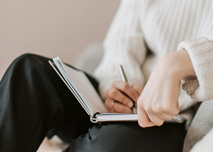 Person in a cozy sweater writing in a notebook, possibly noting unsolved mysteries.