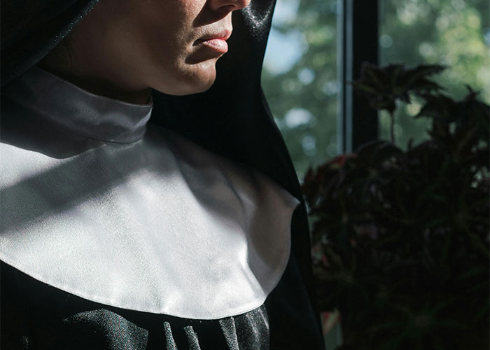 A nun in partial sunlight, wearing a black and white habit, symbolizing unsolved mysteries.