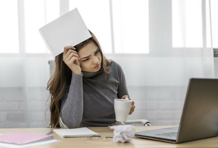 Woman in gray sweater with paper and coffee, contemplating resume red flags while looking at a laptop.