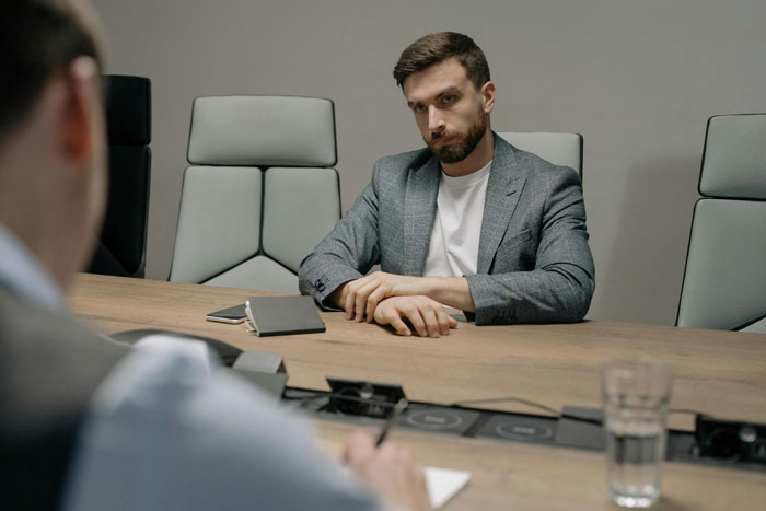 Employee in a meeting room, looking dissatisfied, sitting across from a colleague, highlighting workplace mistreatment.