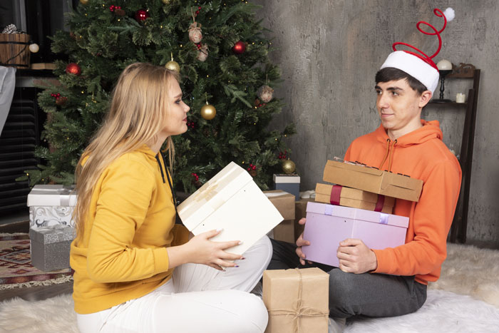 Couple exchanging gifts by a Christmas tree, boyfriend holding Pokémon cards.