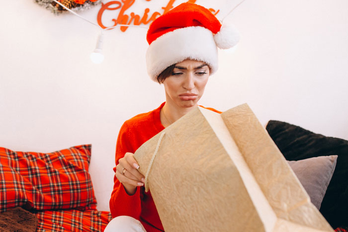 Person in a Santa hat opening a large gift box at Christmas, looking disappointed.