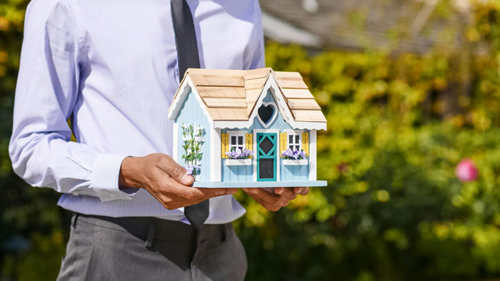 Man in a business shirt holding a small model house, representing mortgage concerns.