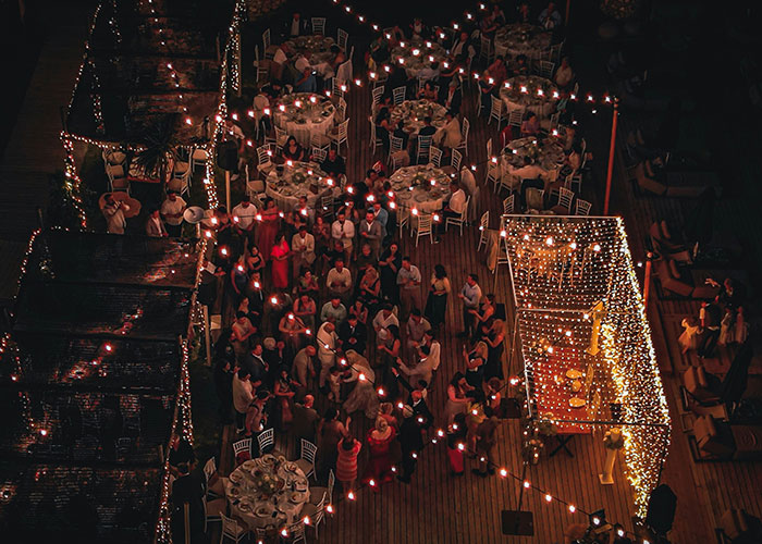 Aerial view of a wedding reception with guests dining and dancing under string lights.