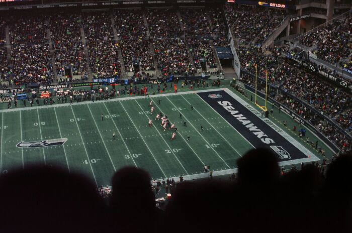 Seattle Seahawks football game in a packed stadium, players lining up on the field, a delivery story atmosphere.