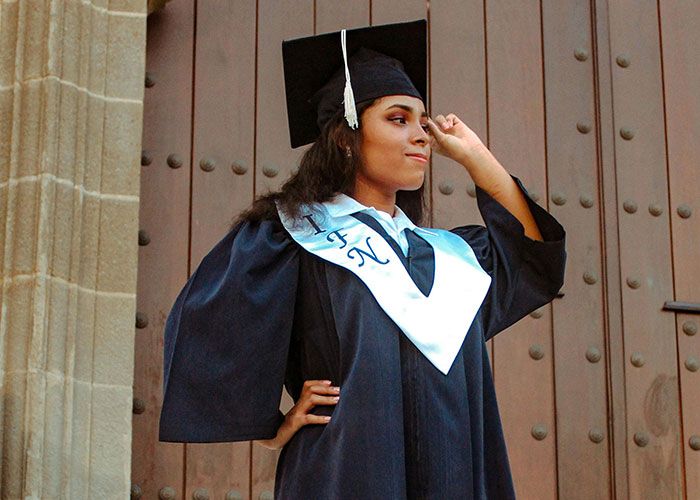 Young graduate in cap and gown, standing confidently in front of a wooden door, symbolizing university achievement.