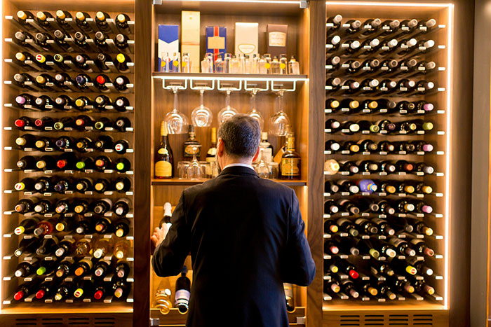 Retail worker organizing wine bottles in a well-lit cellar, showcasing an array of wines neatly arranged on wooden shelves.