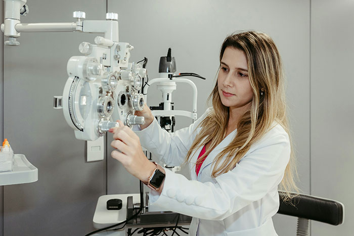 Retail worker adjusting an eye test machine, focused and wearing a white coat.