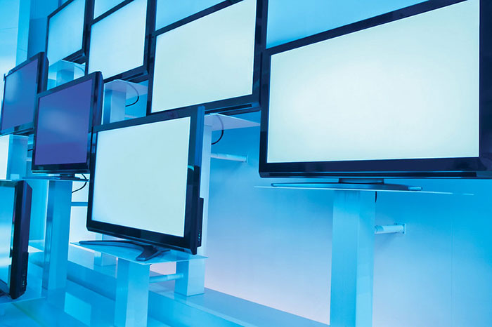 Retail workers' TVs on display with blue lighting in an electronics store.