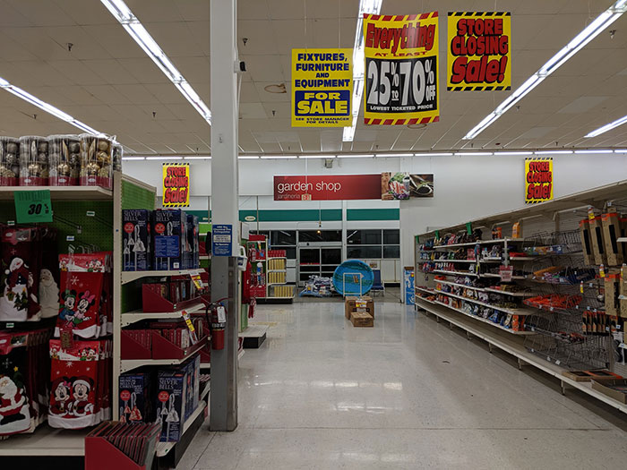 Retail store aisle with clearance and closing sale signs hanging above.