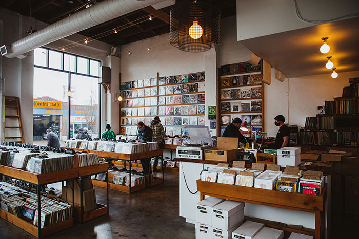 Retail workers in a cozy record store, organizing vinyl records on shelves and assisting customers.