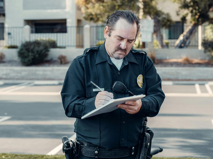 Police officer writing a ticket for a car blocking the driveway.