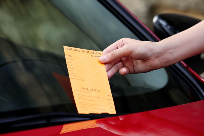 A parking ticket placed on a red car's windshield in a driveway block scenario.