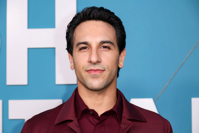 Actor Deniz Akdeniz from High Potential cast in maroon jacket against a blue backdrop.