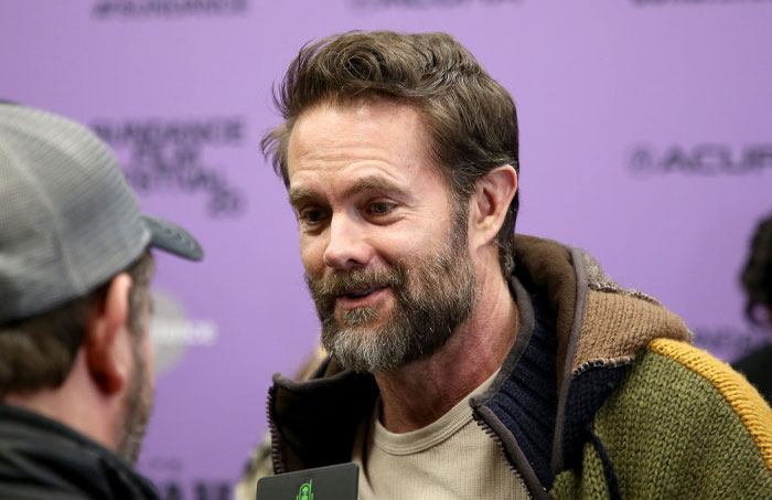 Actor Garret Dillahunt in conversation at an event, wearing a multicolored jacket, representing the cast of High Potential.