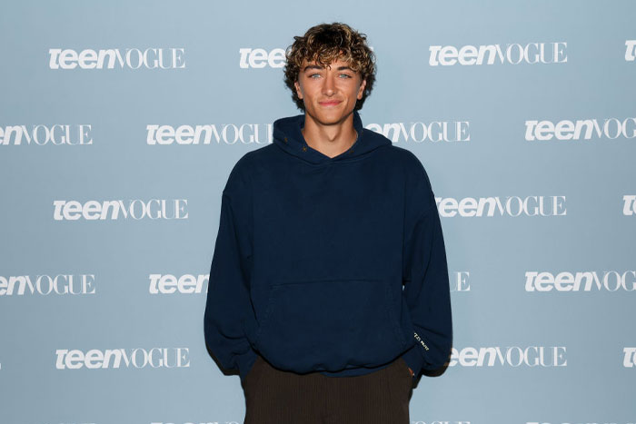 Gavin Casalegno from The Summer I Turned Pretty at a Teen Vogue event, wearing a navy hoodie against a branded backdrop.