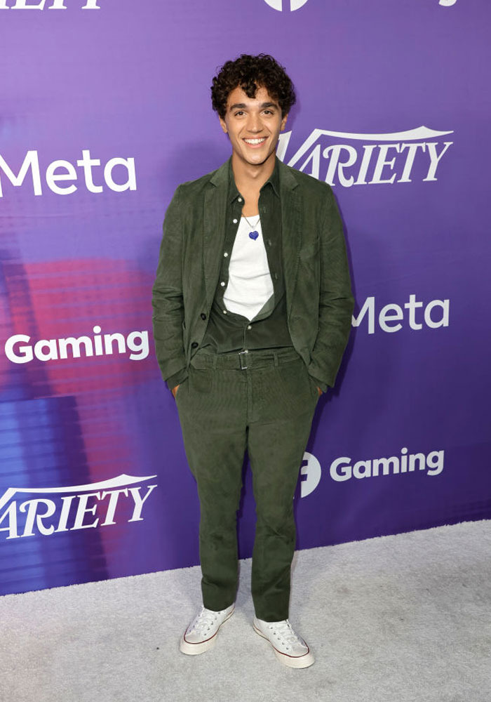 David Iacono from "The Summer I Turned Pretty" in a green outfit at a gaming event backdrop.