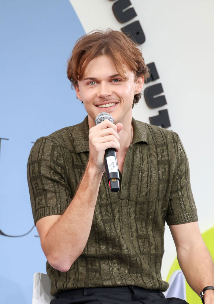 Christopher Briney speaking into a microphone, wearing a green shirt, representing rising stars in The Summer I Turned Pretty.