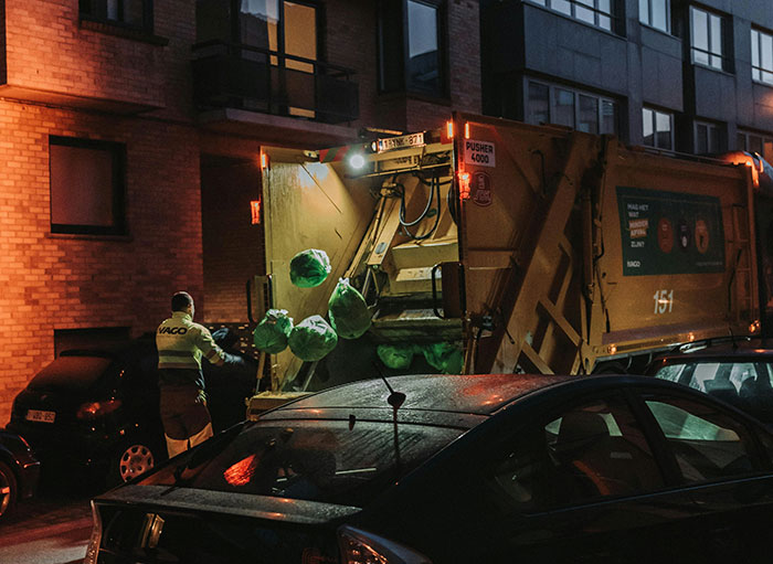 Garbage truck at night with a collector loading bags, illustrating issues with unpaid overtime for waste workers.