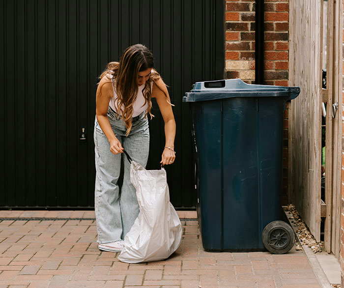 Woman placing garbage in a bin outside, highlighting garbage collection issues.