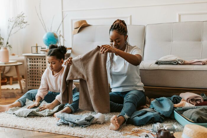 A woman and child folding clothes in a cozy living room, demonstrating clever tips for living cheap comfortably.