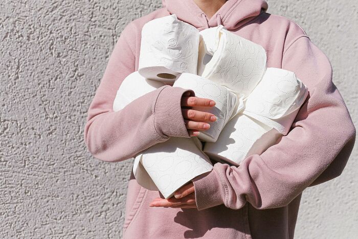 Person in a pink hoodie holding several toilet paper rolls, illustrating tips for living cheap.