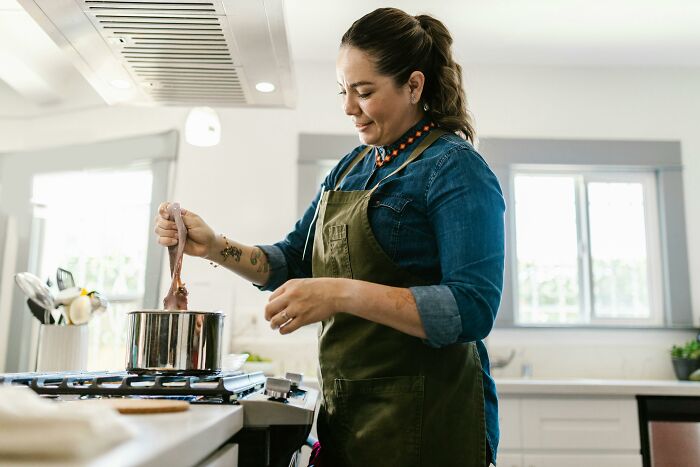 Woman in a kitchen stirring a pot, illustrating clever tips for living cheap while cooking comfortably at home.