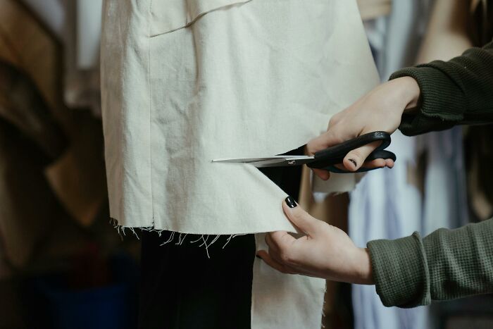 Hands cutting fabric with scissors, demonstrating clever tips for living cheap.