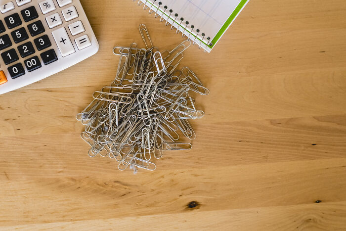 Calculator, paperclips, and notepad on a wooden desk showcasing clever tips for living cheap.