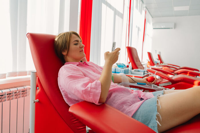 Person donating blood while using a smartphone, illustrating clever tips for living cheap and comfortably.