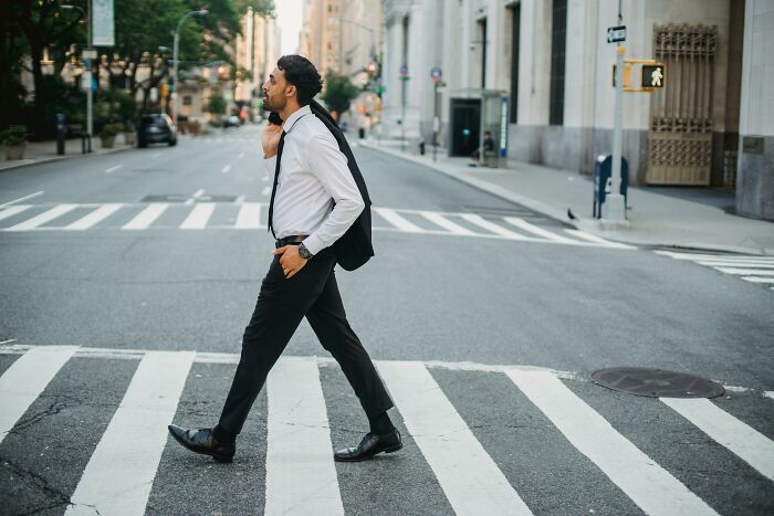 Person in business attire walking on a city street crosswalk, embodying clever tips for living cheap without sacrificing comfort.