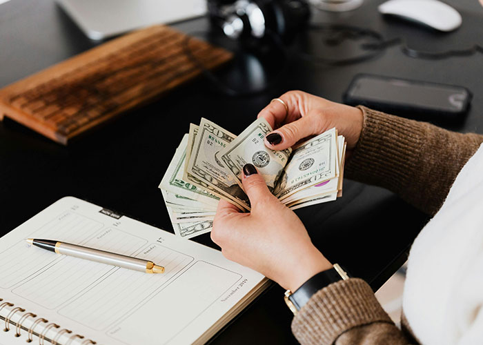 Person counting money at a desk with a notebook and pen, illustrating life cheat codes.