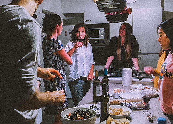 Group of friends sharing life cheat codes, gathered around a kitchen counter with food and wine.